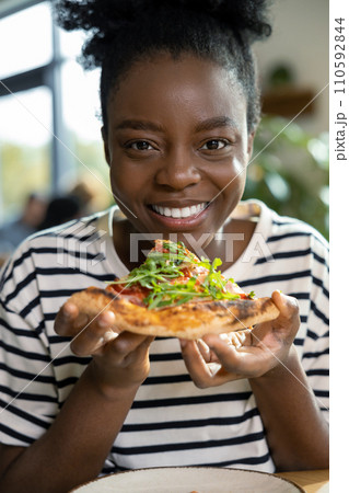 Positive african american woman with a slice of pizza in hands Positive african american woman with a slice of pizza in hands 110592844