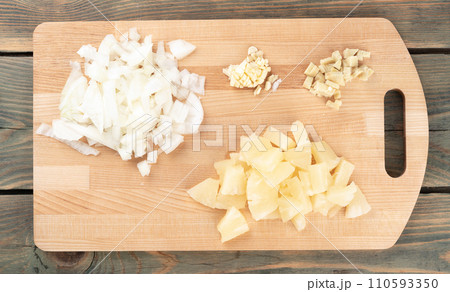 Chopped spices garlic, onions with ginger and pineapple pieces on a cutting board. Chopped spices garlic, onions with ginger and pineapple pieces on a cutting board. 110593350