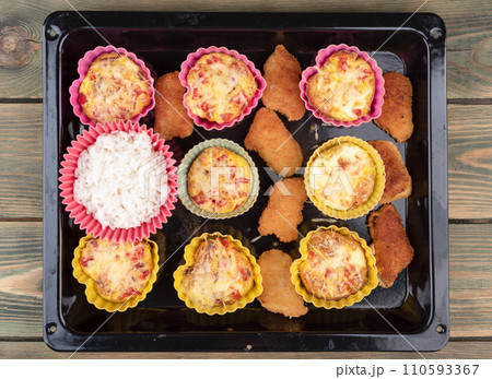 Top view of baked nuggets, filled omelette and rice in baking dishes on a baking sheet. 110593367