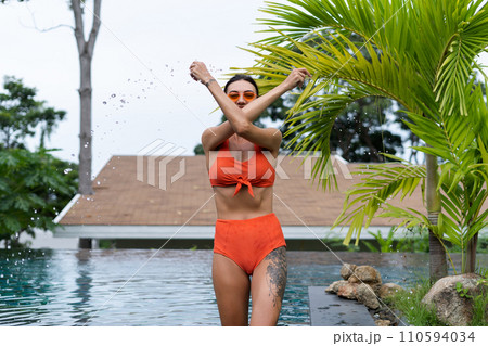 Beautiful european women in two pieces orange bikini swimsuit in perfect shape, good body, tanned, with trendy sunglasses outside at tropical swimming pool and palm leaf tree Beautiful european women in two pieces orange bikini swimsuit in perfect shape, good body, tanned, with trendy sunglasses outside at tropical swimming pool and palm leaf tree 110594034