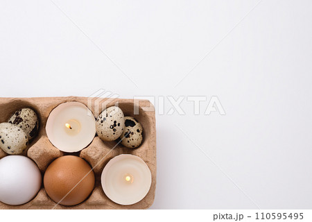 Eggs and candle in eggshell in tray on white background. Quail and chicken eggs. Copy space. Easter holiday concept 110595495