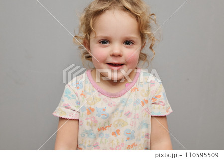 Portrait of smiling cute little toddler blond wavy haired girl child isolated over gray background looking at camera expressing happiness smiling with with cheerful face 110595509