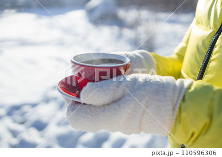 Close up of woman hands with gloves holding coffee mug in winter morning in a park. Hot and warming drinks in the winter concept. Hands close up. 110596306