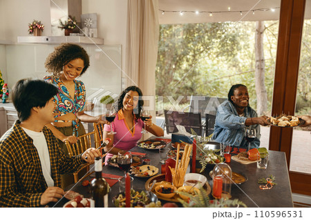 Group of smiling friends enjoying in conversation and drinking wine during Christmas party at home 110596531