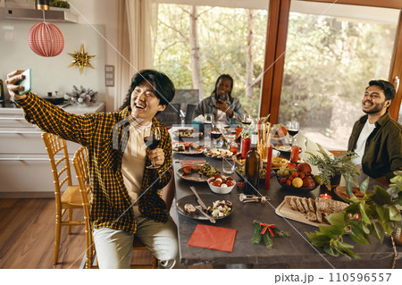 Smiling young friends taking selfie photo holding wine glasses on holiday dinner party at home 110596557