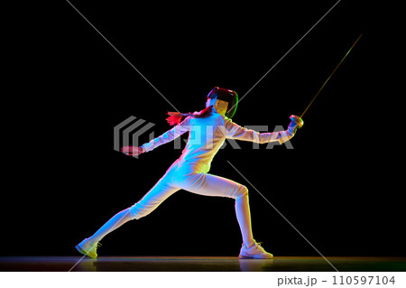Self-defense skills. Although sportive, fencing skills can represent the broader theme of self-defense. Female athlete in motion, training over black background in neon. 110597104