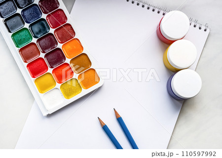 Colorful watercolor or acrylic paints and pencils on a white sheet of paper on a white background. Design studio table top view. Space for text. Colorful watercolor or acrylic paints and pencils on a white sheet of paper on a white background. Design studio table top view. Space for text. 110597992