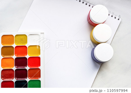 Colorful watercolor or acrylic paints and pencils on a white sheet of paper on a white background. Design studio table top view. Space for text. Colorful watercolor or acrylic paints and pencils on a white sheet of paper on a white background. Design studio table top view. Space for text. 110597994
