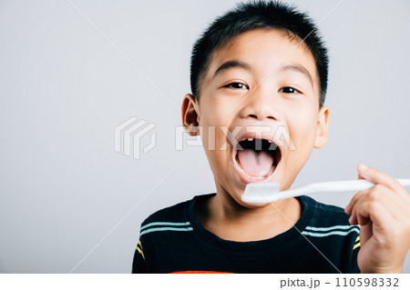 Isolated on a white background an Asian child without an upper milk tooth holds a toothbrush promoting dental hygiene routine and the joy of learning with a cheerful smile. Children dentist routine 110598332