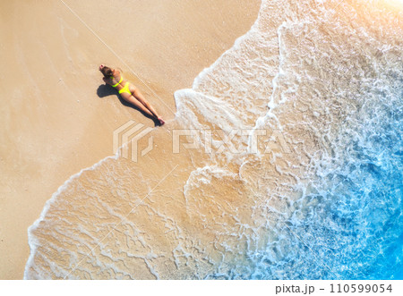 Aerial view of the young lying woman on the sandy beach near sea 110599054