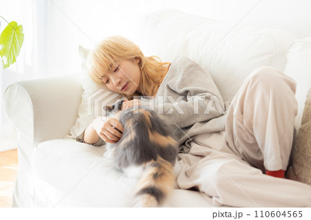 ソファーに寝転び猫を抱っこする日本人女性 110604565