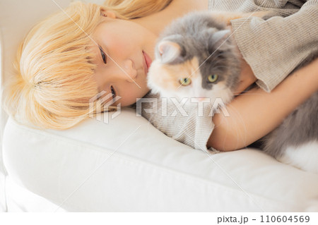 ソファーに寝転び猫を抱っこする日本人女性 110604569