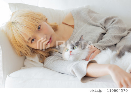 ソファーに寝転び猫を抱っこする日本人女性 110604570