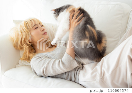 ソファーに寝転び猫を抱っこする日本人女性 ソファーに寝転び猫を抱っこする日本人女性 110604574