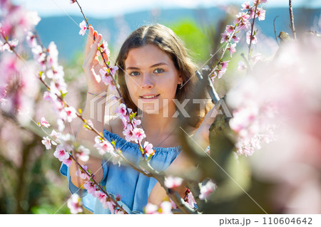 Young smiling lady posing in park with blooming trees Young smiling lady posing in park with blooming trees 110604642