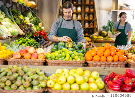 Male seller laying out ripe bell peppers on a showcase in supermarket 110604686