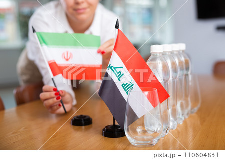 Woman secretary prepares an office for negotiations - she places flags of Iraq and Iran table 110604831