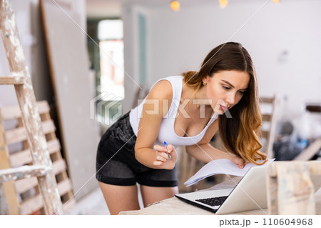 Young attractive girl checks the quality and correctness of the completed repairs using a laptop inside cottage 110604968