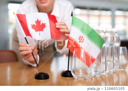 Little flag of Iran on table and flag of Canada put next to it by young woman Little flag of Iran on table and flag of Canada put next to it by young woman 110605105