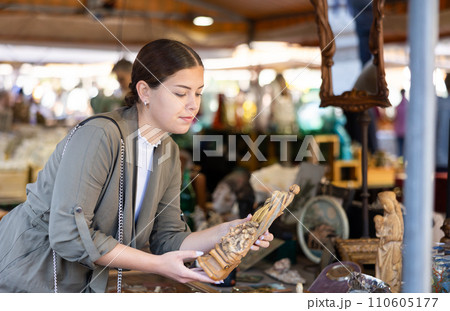 Happy female tourist looking to buy handmade wooden statue at flea market Happy female tourist looking to buy handmade wooden statue at flea market 110605177