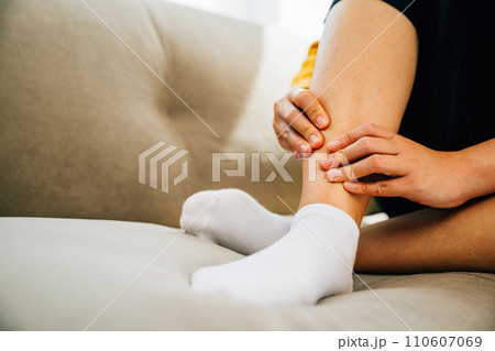 Illustrating health care concept, woman sits on sofa holding her painful ankle. Emphasizing varicose vein prevention leg recovery and pain management for the patient. medical Illustrating health care concept, woman sits on sofa holding her painful ankle. Emphasizing varicose vein prevention leg recovery and pain management for the patient. medical 110607069