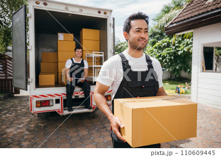 Young delivery men unload boxes outdoors. Movers cooperate in relocation service. Teamwork among colleagues. Smiling workers carrying boxes. relocation cooperation Moving Day 110609445