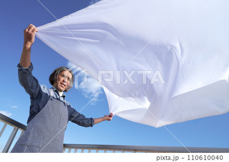 青空のもとで洗濯物のシーツを広げるミドル男性 110610040