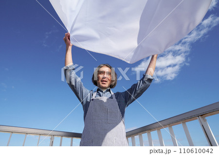 青空のもとで洗濯物のシーツを広げるミドル男性 110610042