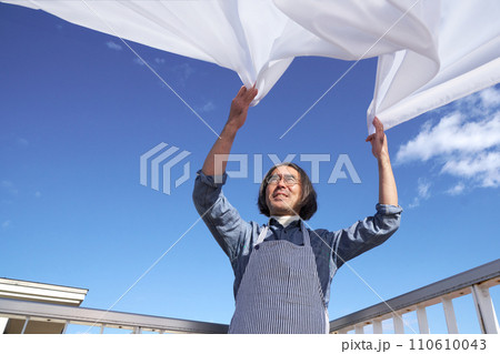 青空のもとで洗濯物のシーツを広げるミドル主夫 110610043