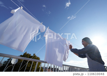 青空のもとで洗濯物のTシャツをロープに干す男性 青空のもとで洗濯物のTシャツをロープに干す男性 110610048