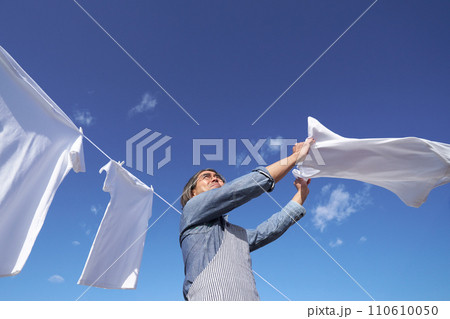 青空のもとで洗濯物のシャツを広げる専業主夫 110610050