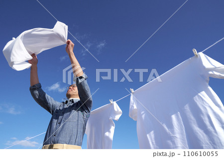 青空のもとで洗濯物のシャツを広げる専業主夫 110610055