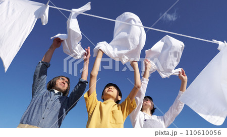 青空のもと並んで洗濯物を干す3人家族 110610056