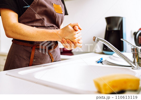 Unrecognizable female figure in brown work apron in kitchen near kitchen sink Unrecognizable female figure in brown work apron in kitchen near kitchen sink 110613119