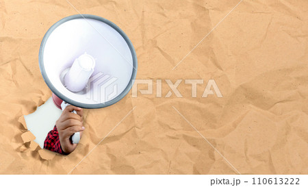 A human hand holding a megaphone comes out from the torn paper A human hand holding a megaphone comes out from the torn paper 110613222