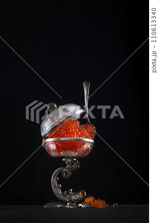 Red caviar. Caviar in the caviar bowl. A spoon for caviar. Beautiful vintage tableware. Black background. Vertical photo. Copy space. 110613340