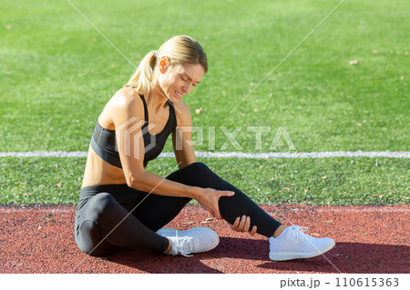 Fitness enthusiast feeling discomfort in her leg on the track field, indicating a potential injury or strain. 110615363