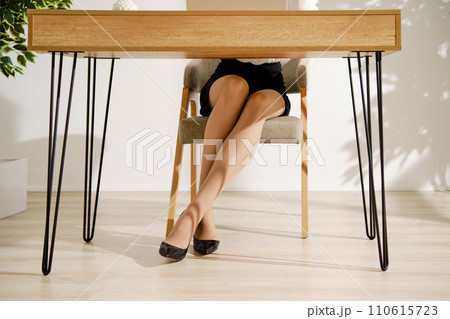 Crossed female legs in thin beige pantyhose under the office table 110615723