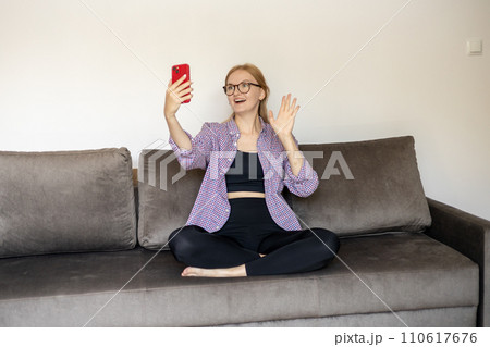 Young beautiful happy girl in glasses say Hi. Attractive Woman using smart phone app over room background, online communication concept. 30s Women taking selfie 110617676