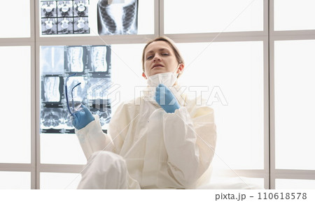 Tired doctor in protective suit sits on floor with X-rays hanging in background Tired doctor in protective suit sits on floor with X-rays hanging in background 110618578