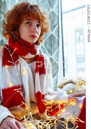 red-haired teenage girl decorates house with festive garland with light bulbs red-haired teenage girl decorates house with festive garland with light bulbs 110619701