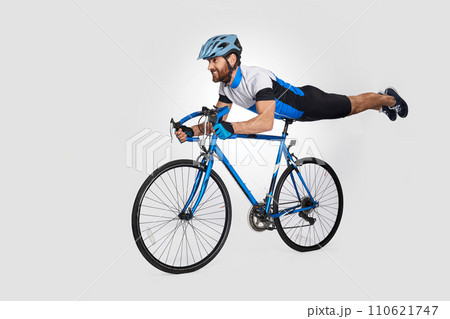 Strong middle aged cyclist doing trick on bike, while riding. Side view of caucasian male rider cyclist showing acrobatic stunt, isolated on white background. Cycling skills, sport activity concept. 110621747