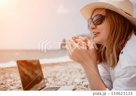 Woman sea laptop. Business woman in yellow hat working on laptop by sea. Close up on hands of pretty lady typing on computer outdoors summer day. Freelance, digital nomad, travel and holidays concept. 110623133