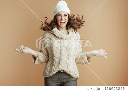 smiling trendy woman in beige sweater, mittens and hat jumping 110623246