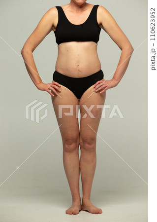 Full-length figures of a fifty-year-old woman in black lingerie on a gray background. Full-length figures of a fifty-year-old woman in black lingerie on a gray background. 110623952