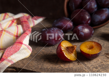 Whole and half of purple plums on wooden background. . 110624230