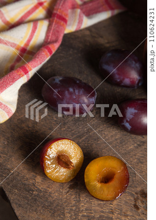 Whole and half of purple plums on wooden background. . 110624231