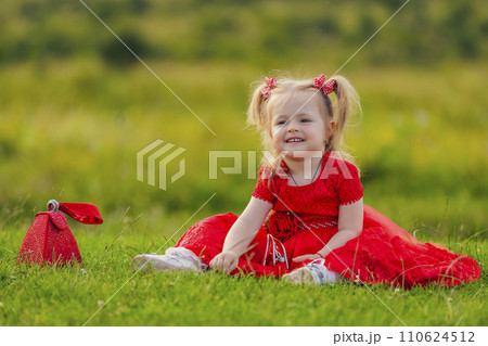 little girl in a red dress sitting on the lawn 110624512