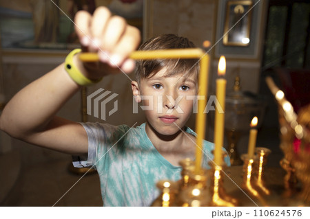 A boy lights candles in an Orthodox church. 110624576