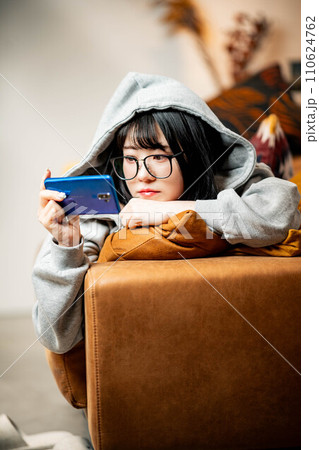 ソファーに寝転びスマホをいじる女性 110624762